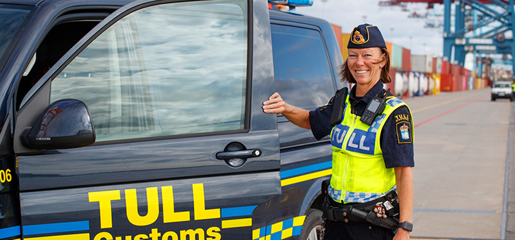 Tullinspektör står utomhus intill en tjänstebil.
