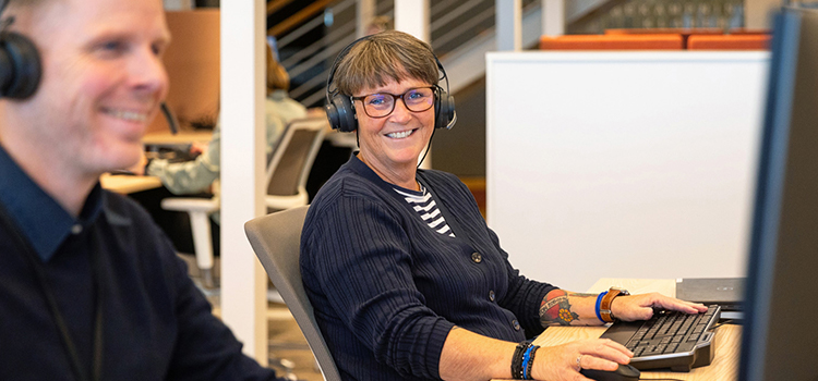 Två personer med hörlurar sitter arbetar framför varsin dator.