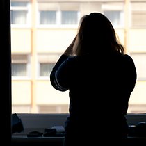 En siluettbild av en kvinna som står mot ett fönster och ryggen mot kameran.