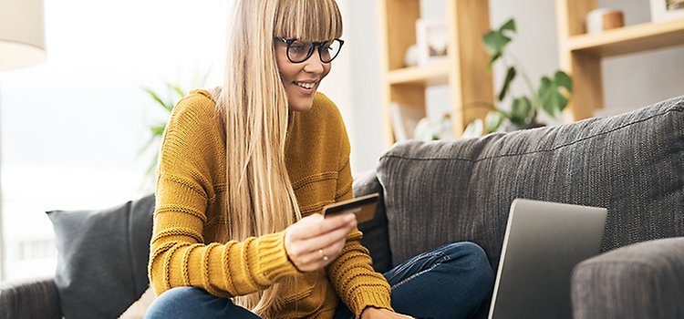 En kvinna i gul tröja sitter framför en bärbar dator och shoppar online.