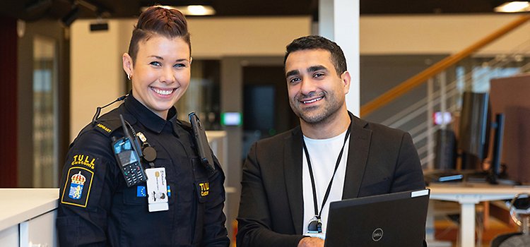 Två glada personer står upp i ett kontorslandskap och tittar in i kameran. Foto: Mette Ottosson